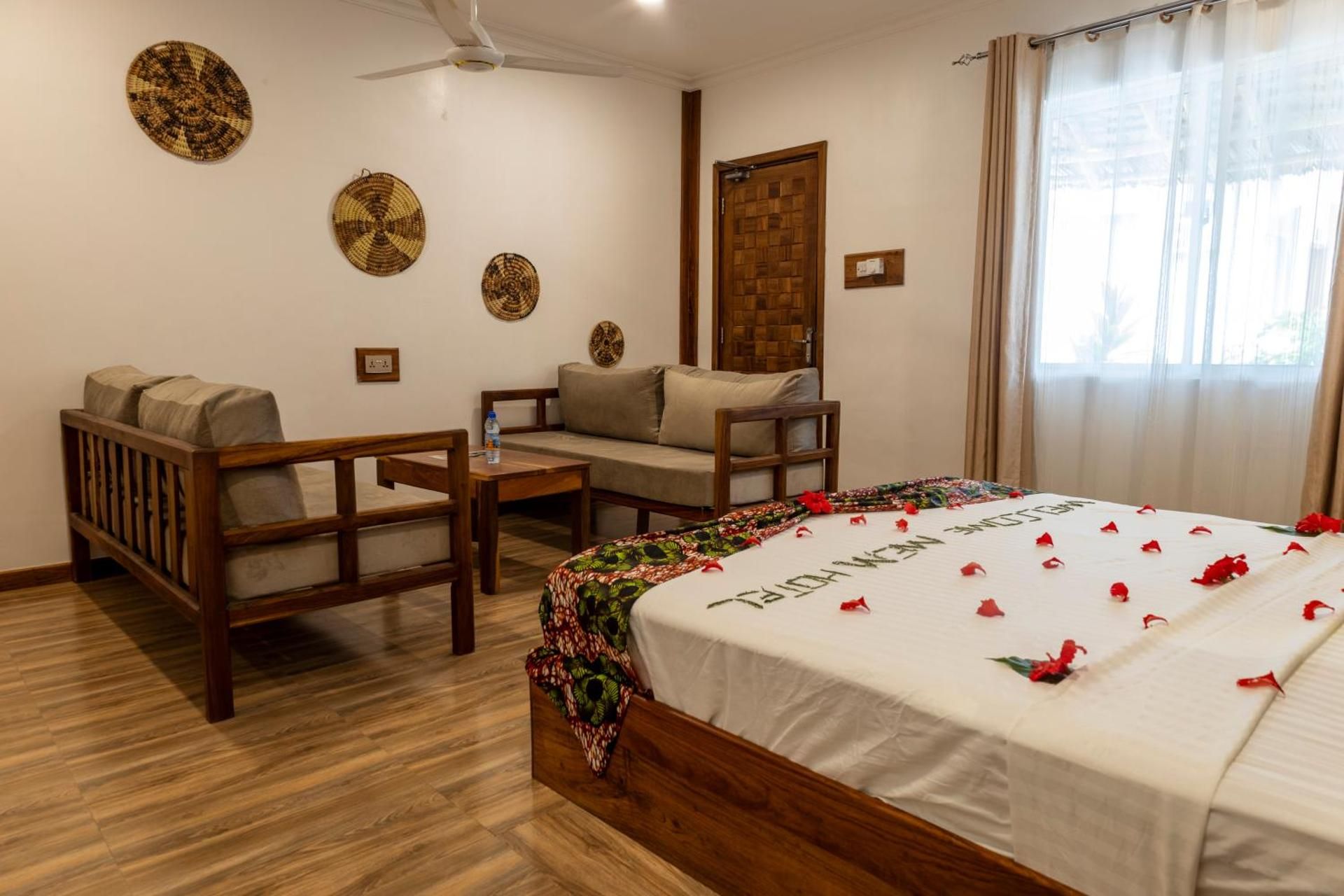 Comfort Quadruple Room: a king bed scattered with petals, a lounge corner and woven baskets on the wall.