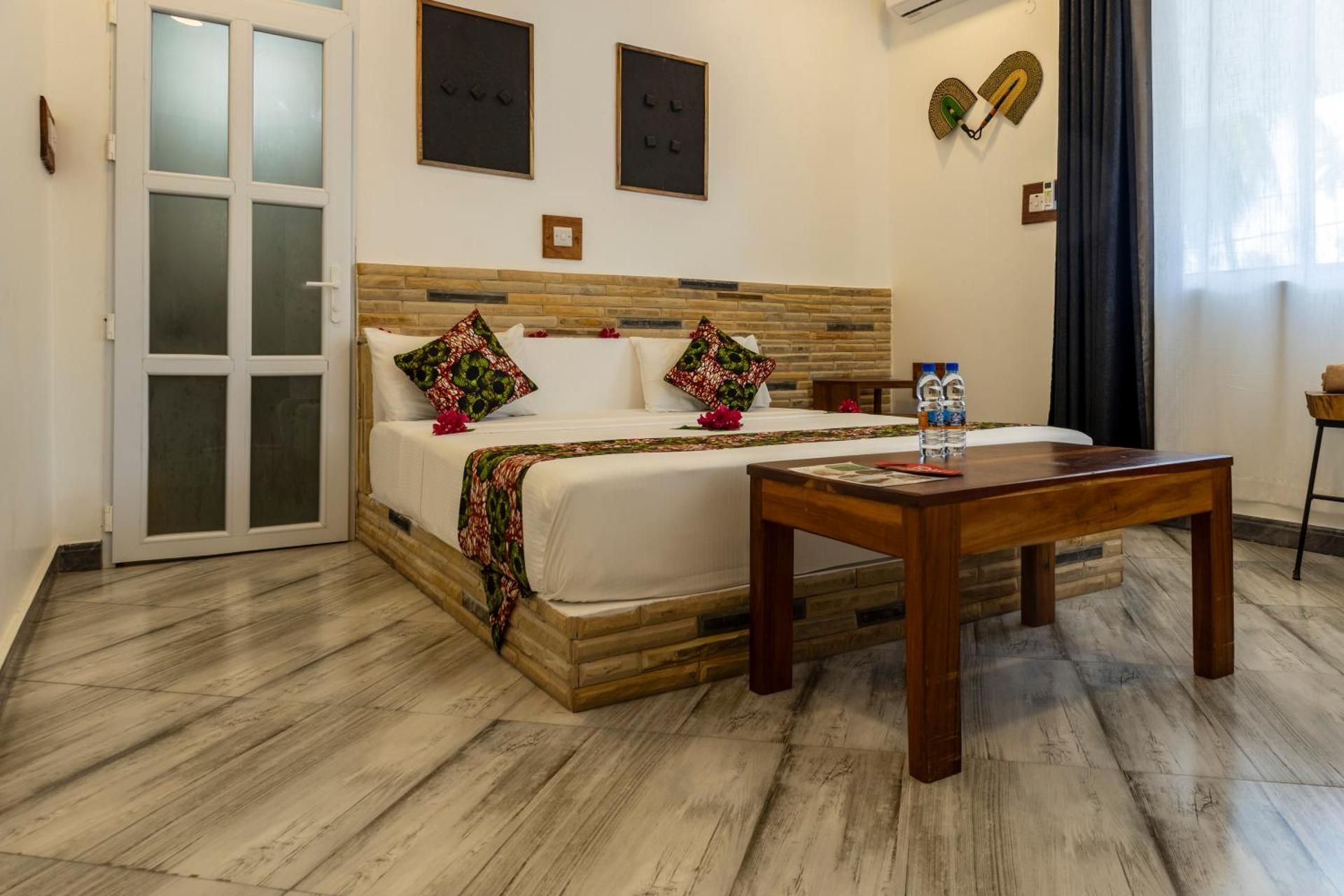 Deluxe Room: a king bed against a stone-tile headboard, with a low wooden table and bottled water.