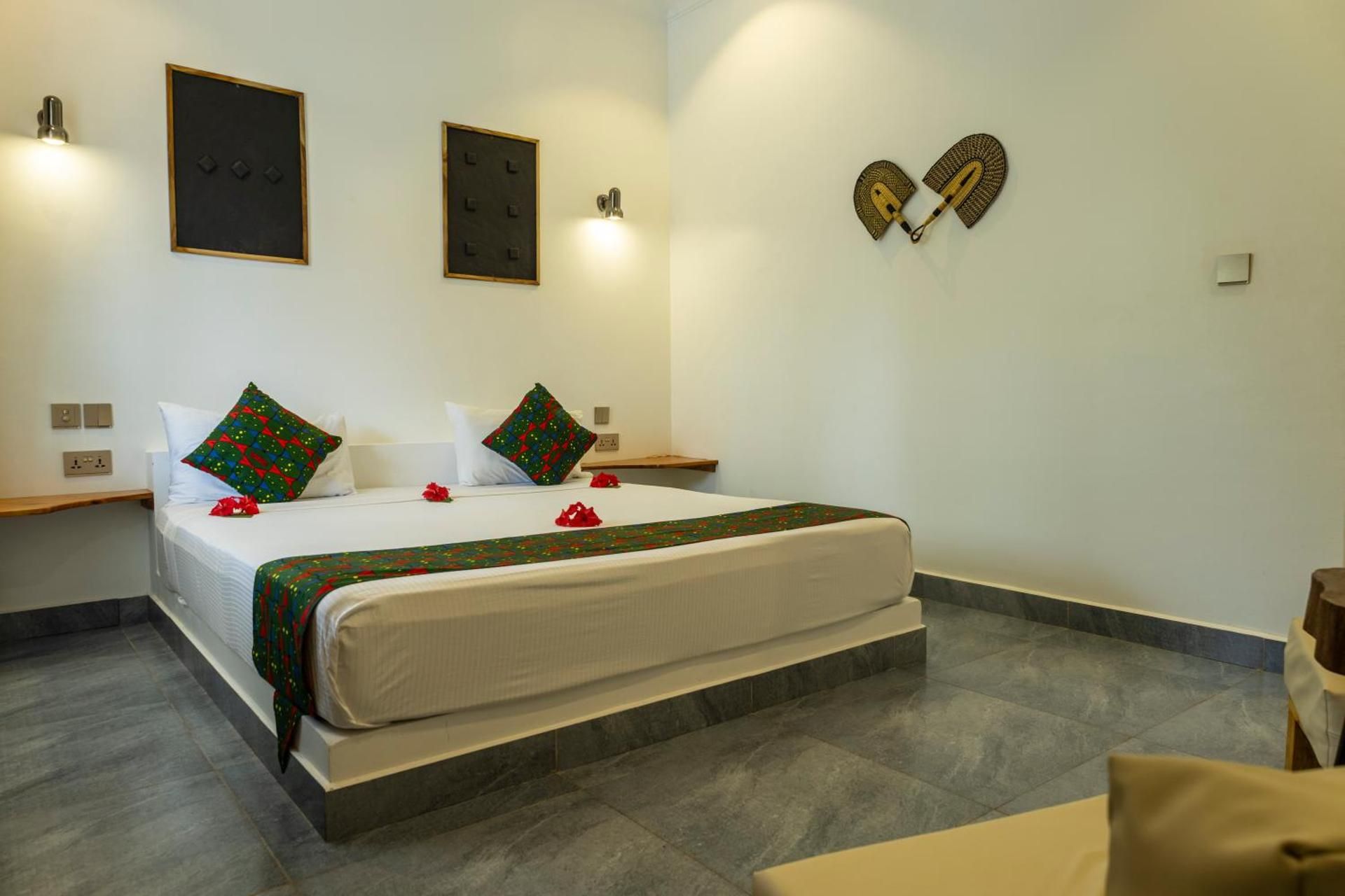 Queen Suite: a king bed with kitenge cushions and hibiscus petals, dark wall panels and two wall lamps.