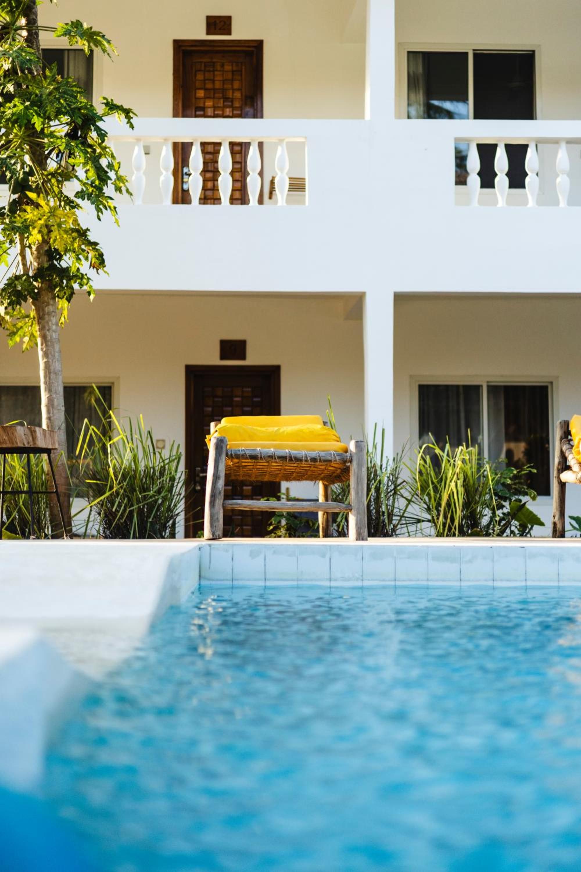 The pool beside the white building with its balconies, yellow loungers along the edge.