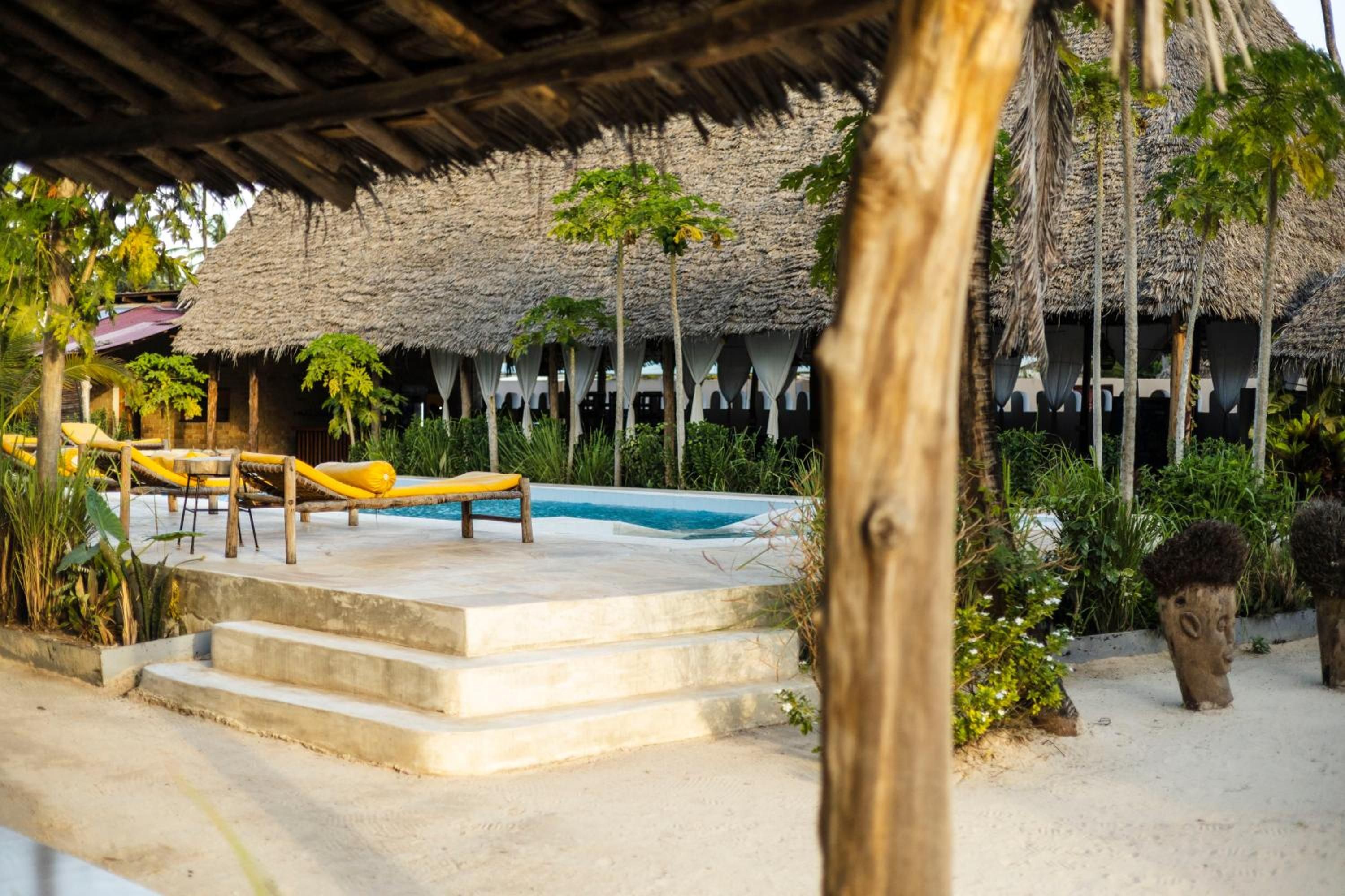 A raised wooden lounger on white steps by the small pool, under a makuti-thatched pavilion.