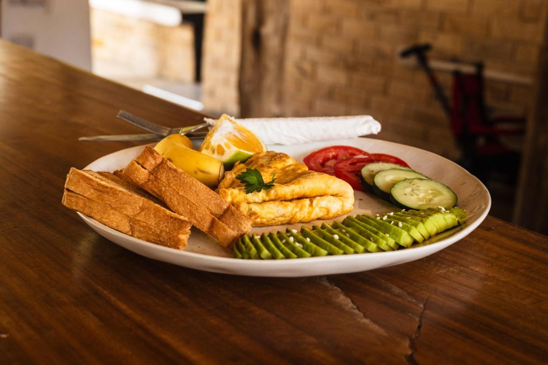 Breakfast plate: an omelette, toast, cucumber and tomato on a wooden table.